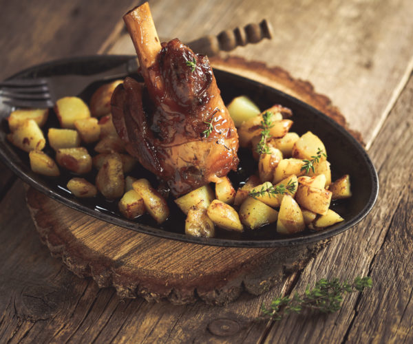 Souris d'agneau rôtie sur des pommes de terres poêlées dans une assiette ronde qui elle-même est sur une tranche de tronx d'arbre au restaurant la table de trois à Bordeaux